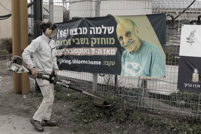 KISSUFIM, ISRAEL - FEBRUARY 11: A woman works near a sign with a photo of hostage Shlomo Mansour, after the Israeli army has confirmed that Mansour was killed on Oct 7 deadly attack, and his body was taken to the Gaza Strip at the entrance to his kibbutz on February 11, 2025 in Kissufim, Israel. On Monday, a Hamas spokesperson accused Israel of violating the terms of the current ceasefire agreement and said it will delay further release of Israeli hostages, until its concerns are resolved. In response, the Israeli PM said the country will take "determined and relentless action until we return all of our hostages."