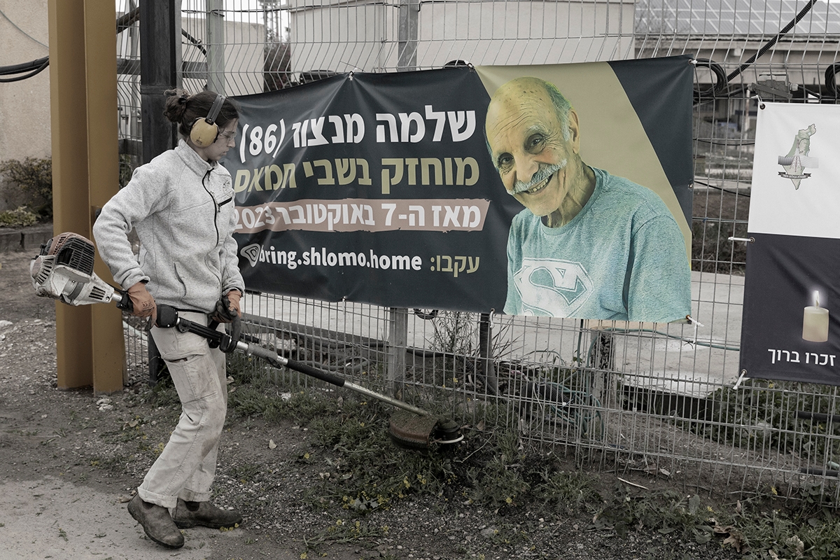 KISSUFIM, ISRAEL - FEBRUARY 11: A woman works near a sign with a photo of hostage Shlomo Mansour, after the Israeli army has confirmed that Mansour was killed on Oct 7 deadly attack, and his body was taken to the Gaza Strip at the entrance to his kibbutz on February 11, 2025 in Kissufim, Israel. On Monday, a Hamas spokesperson accused Israel of violating the terms of the current ceasefire agreement and said it will delay further release of Israeli hostages, until its concerns are resolved. In response, the Israeli PM said the country will take "determined and relentless action until we return all of our hostages."